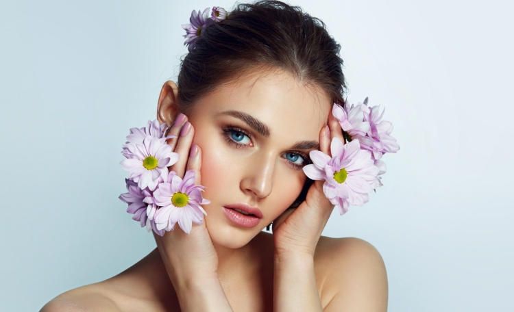 Zabiegi kosmetyczne na wiosnę - piękna, młoda kobieta przykładająca do twarzy kwiaty